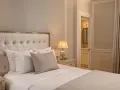 Elegancka sypialnia z pikowanym zagłówkiem, dwoma lampkami nocnymi i widokiem na łazienkę. Idealne miejsce dla wynajmującego szukającego komfortu.