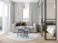 Jasna, nowoczesna kawalerka z wydzieloną sypialnią za szklaną ścianką. W salonie sofa, stoliki i okrągły dywan.