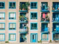 Elegancka loggia i balkon z niebieskimi ramami okiennymi, pełne zieleni i suszącego się prania, tworzą kolorowy wzór na fasadzie budynku.