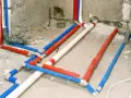 Skomplikowana instalacja cwu z rurami w kolorach czerwonym, niebieskim i białym, prowadząca do przyszłej łazienki.