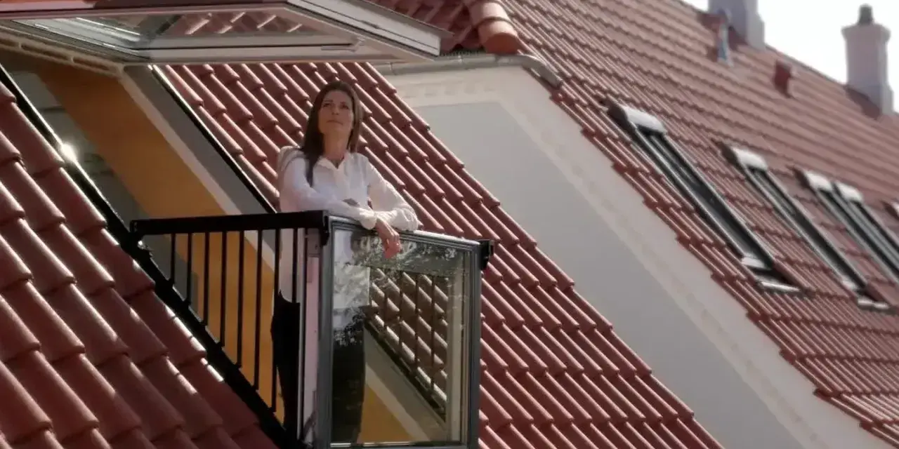 Kobieta na balkonie wychodzącym z okienka w dachu, podziwia widok.