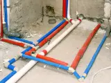 Skomplikowana instalacja cwu z rurami w kolorach czerwonym, niebieskim i białym, prowadząca do przyszłej łazienki.