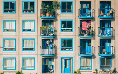 Elegancka loggia i balkon z niebieskimi ramami okiennymi, pełne zieleni i suszącego się prania, tworzą kolorowy wzór na fasadzie budynku.