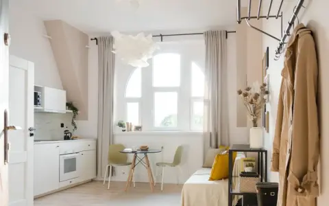 Jasne, przytulne mieszkanie idealne na najem okazjonalny. Biała kuchnia, okno z zasłonami, stolik z krzesłami i wygodna kanapa.