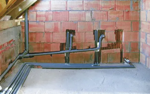 Instalacja hydrauliczna w trakcie budowy, z widocznym systemem rur i pionów, przygotowana do podłączenia odpowietrzenia kanalizacji.