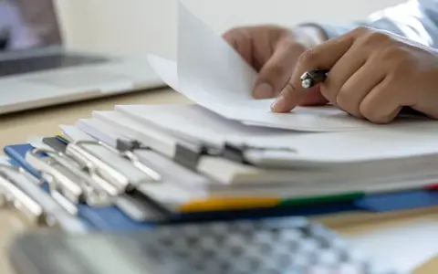 Ręce przeglądają dokumenty, szukając informacji, kiedy można wymeldować członka rodziny.