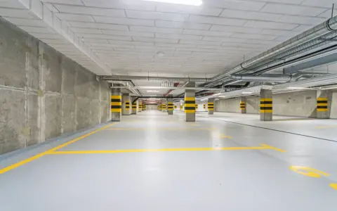 Pusty garaż podziemny z żółtymi liniami parkingowymi i betonowymi słupami w czarno-żółte pasy.