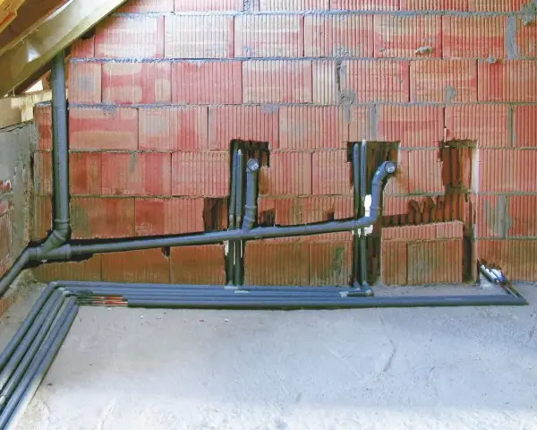 Instalacja hydrauliczna w trakcie budowy, z widocznym systemem rur i pionów, przygotowana do podłączenia odpowietrzenia kanalizacji.