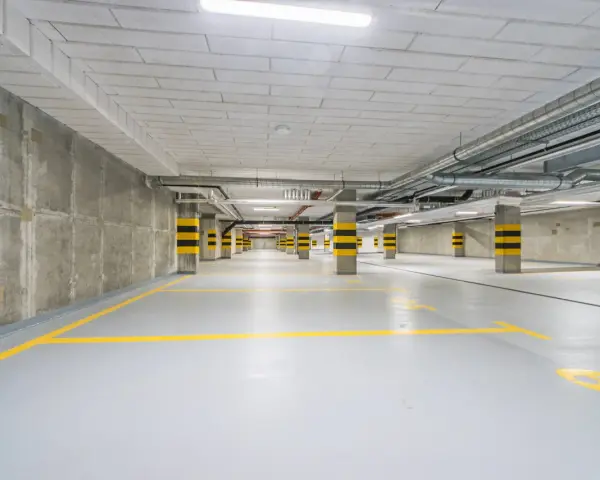 Pusty garaż podziemny z żółtymi liniami parkingowymi i betonowymi słupami w czarno-żółte pasy.