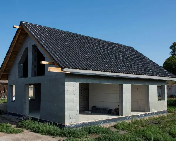 Dom w stanie surowym otwartym, z dachem pokrytym czarną dachówką. Ściany z bloczków betonowych, bez okien i drzwi.