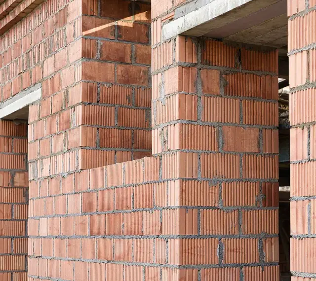 Ściany z pustaków ceramicznych w trakcie budowy. Widoczne różne rodzaje pustaków, tworzące solidną konstrukcję.
