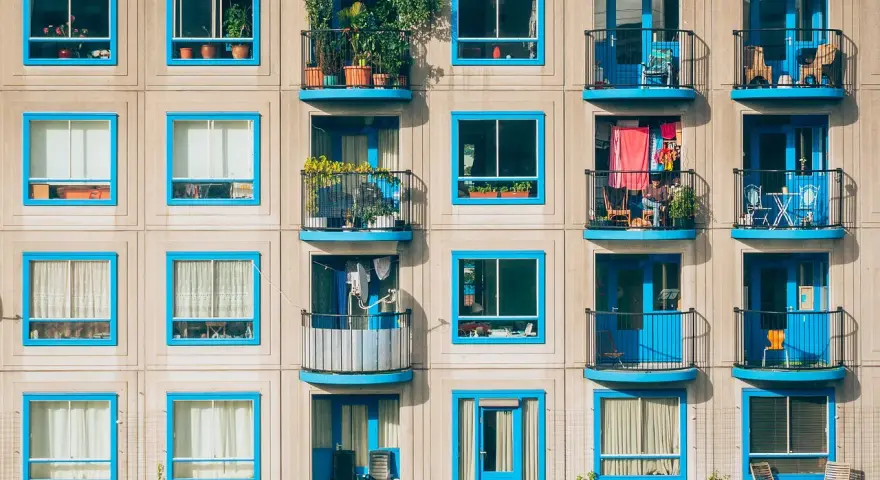 Elegancka loggia i balkon z niebieskimi ramami okiennymi, pełne zieleni i suszącego się prania, tworzą kolorowy wzór na fasadzie budynku.