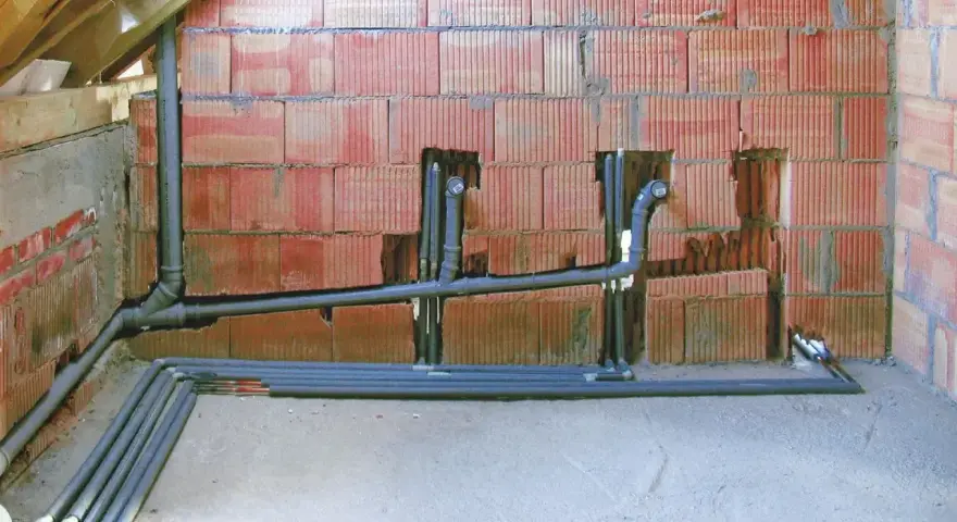 Instalacja hydrauliczna w trakcie budowy, z widocznym systemem rur i pionów, przygotowana do podłączenia odpowietrzenia kanalizacji.